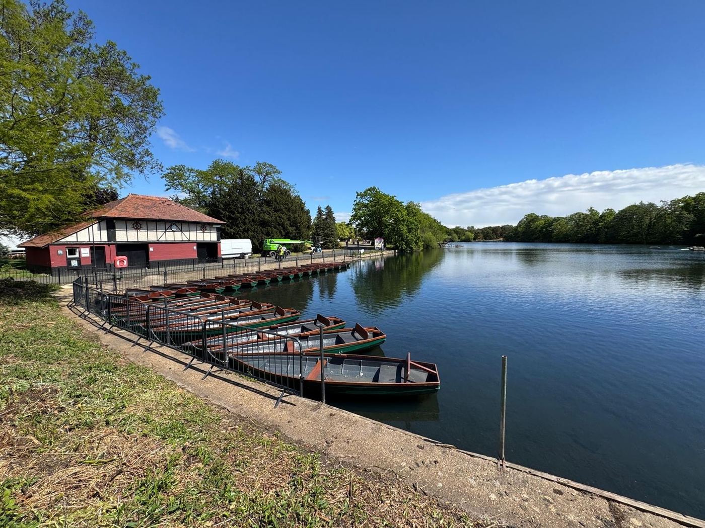 A full row of green rowing boats moored below the boathouse on a sunny day